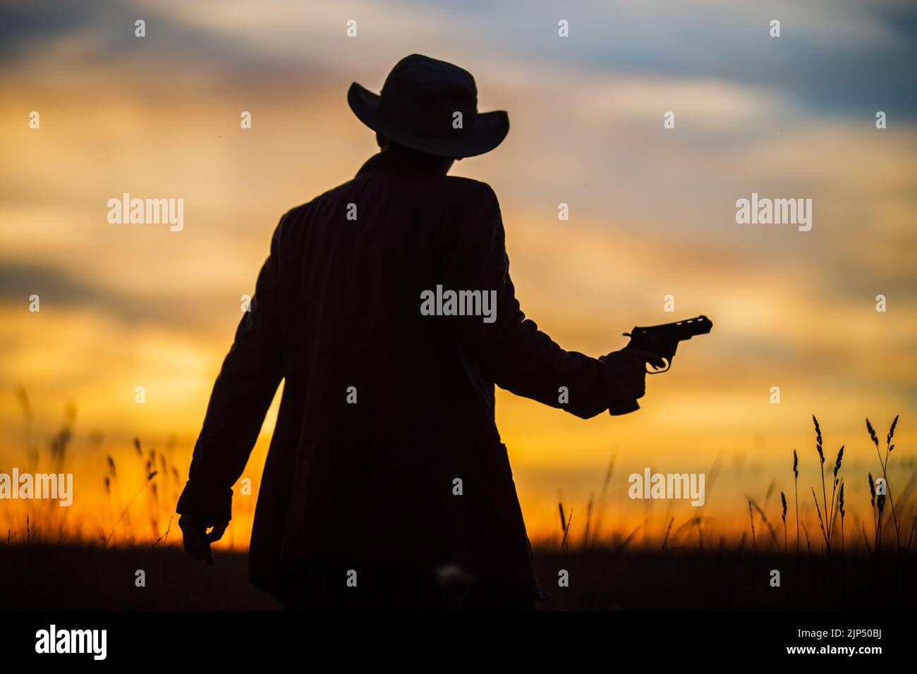 Silhouette di un cowboy in un cappello con una revolver contro un suggestivo cielo al tramonto. Concetto occidentale. Vita nel selvaggio West Foto Stock