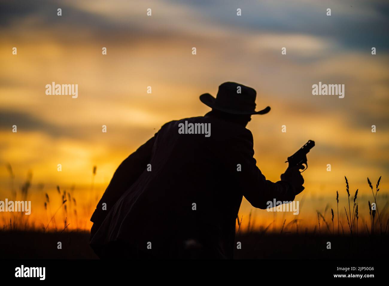 Silhouette di un cowboy in un cappello con una revolver contro un suggestivo cielo al tramonto. Concetto occidentale. Vita nel selvaggio West Foto Stock