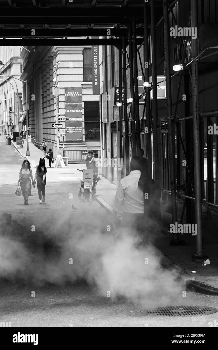 Un'immagine verticale in scala di grigi di una strada a Manhattan con persone che passano da un'area fumosa Foto Stock
