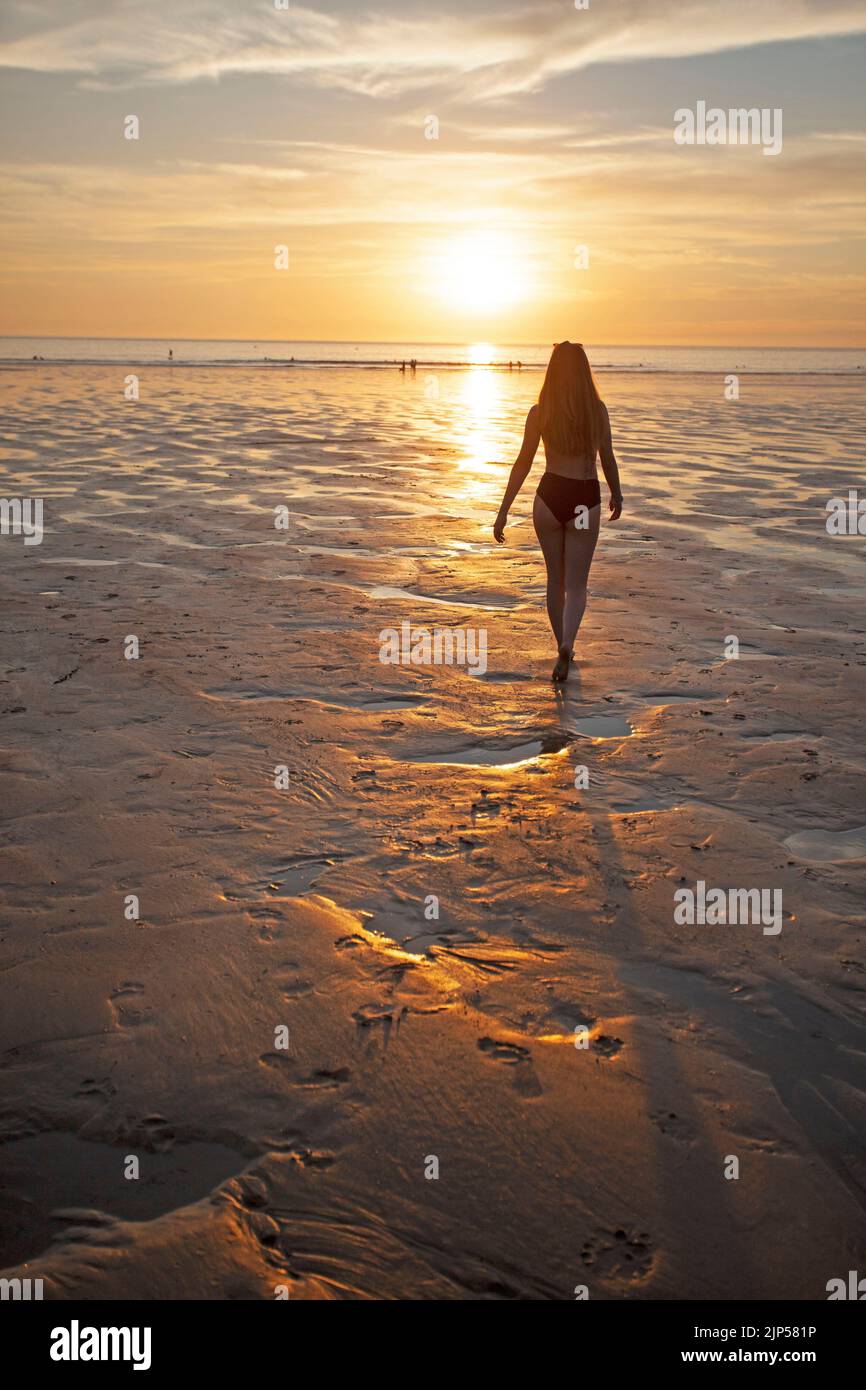 Ragazza giovane che cammina attraverso la spiaggia di Polzeath verso il tramonto. Cornovaglia Inghilterra Foto Stock