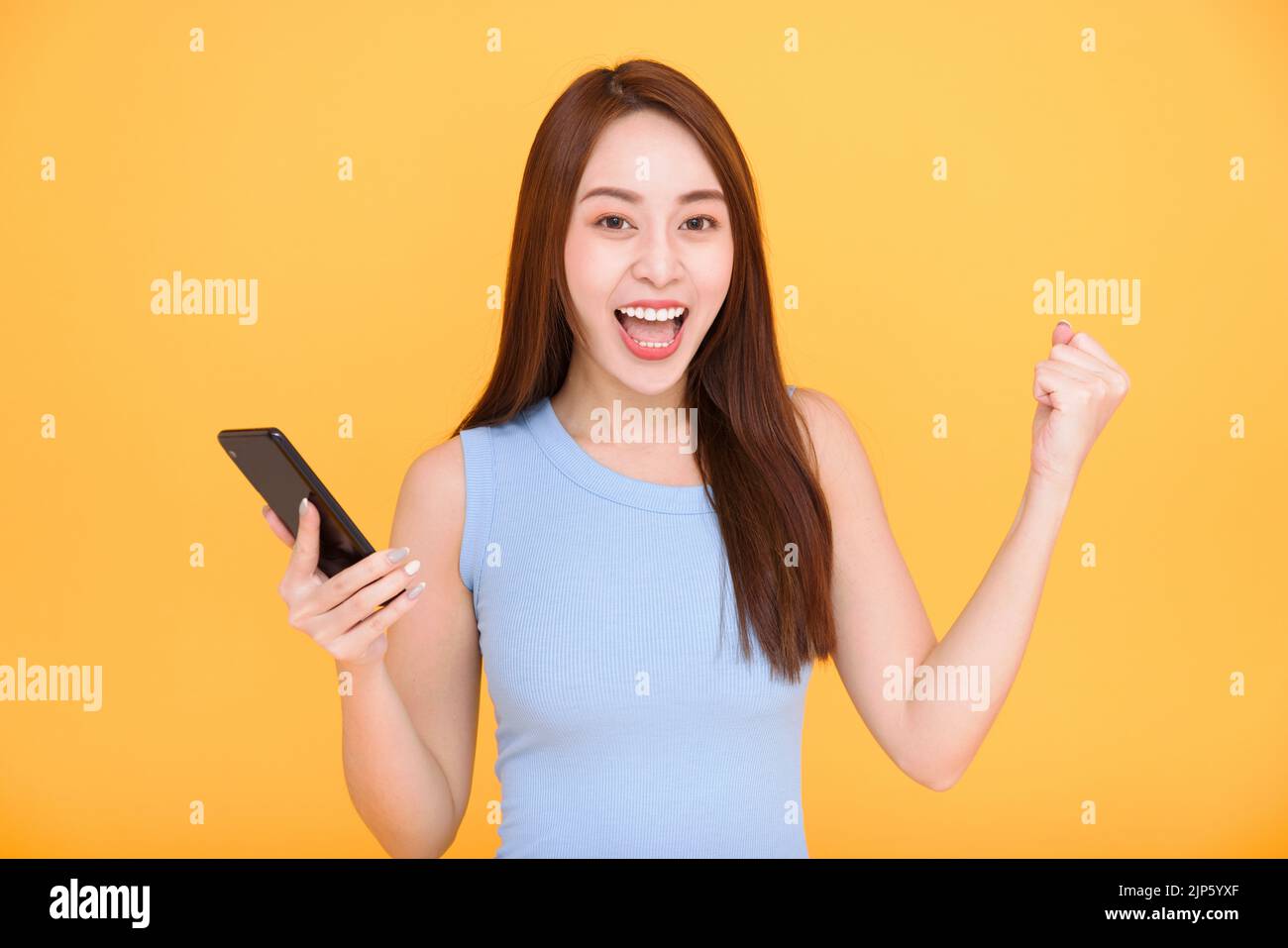 Felice giovane donna che tiene il telefono cellulare e festeggia il successo Foto Stock