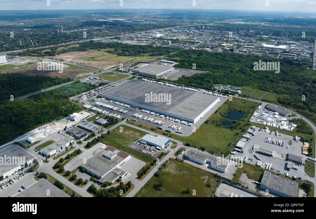 Una vista dall'alto, dall'aspetto di un grande magazzino con rimorchi per trattori ancorati intorno all'edificio. Vista in una vasta zona industriale in una giornata di sole. Foto Stock