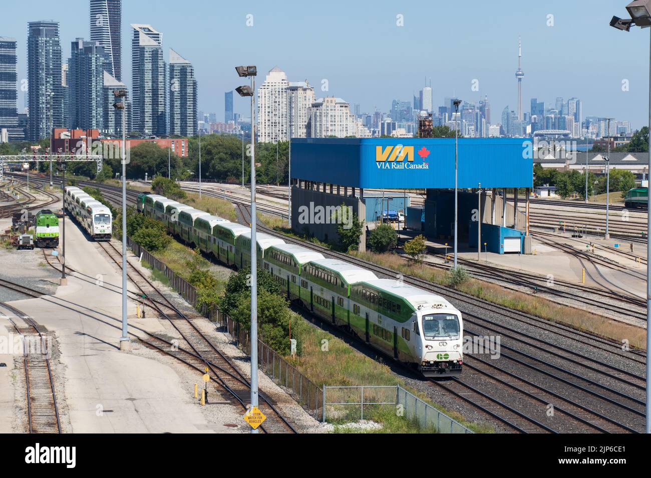 Un treno GO Transit passa attraverso una stazione ferroviaria alla periferia di Toronto, lo skyline della città è visto in lontanità. Foto Stock