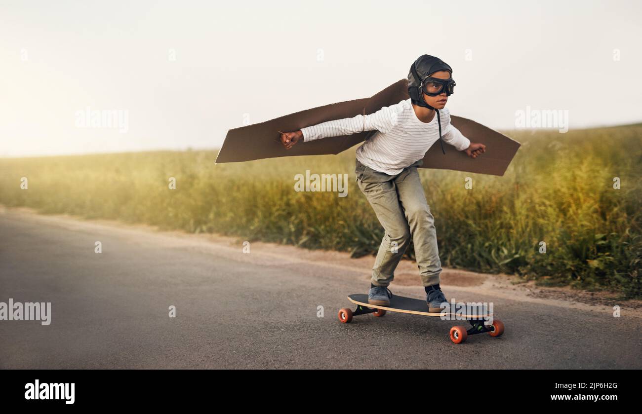 HES ha avuto l'immaginazione più selvaggia. Un ragazzo che finge di volare con un paio di ali di cartone mentre si guida uno skateboard all'esterno. Foto Stock