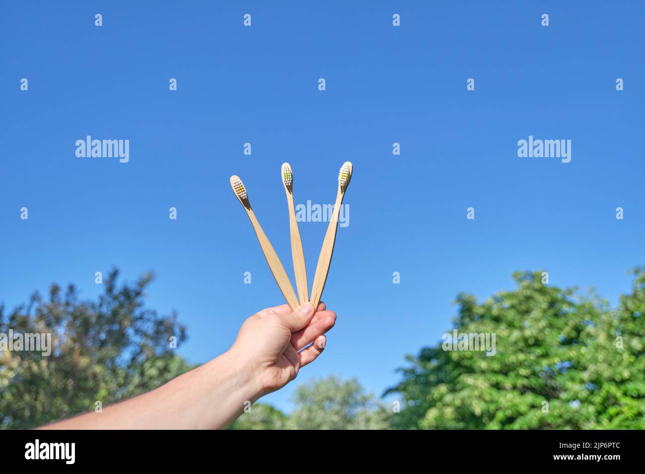 Mano che tiene tre spazzolini ecologici di bambù all'aperto. Concetti: Stile di vita sostenibile, uso di materiali compostabili e rispettosi dell'ambiente Foto Stock