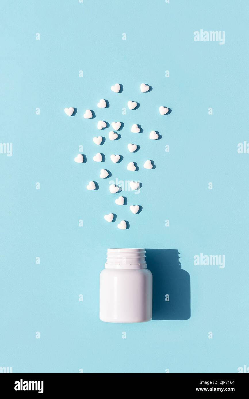 Le pillole bianche a forma di cuore escono dalla bottiglia su sfondo blu. Medicina, concetto di assistenza sanitaria. Vista dall'alto Flat Lay. Foto Stock