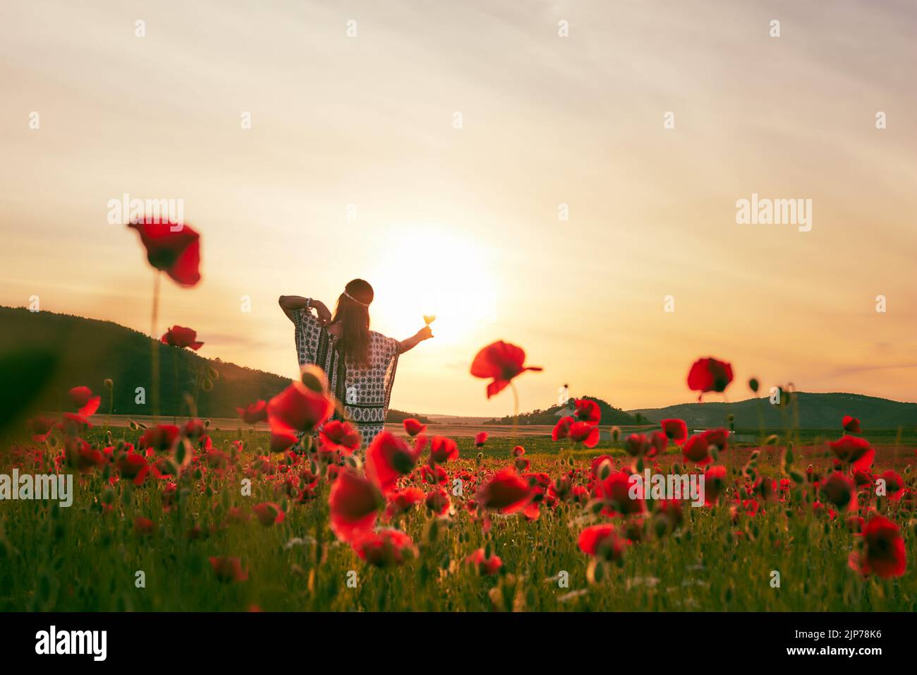 Una donna che mangia fragole al tramonto in un campo di papaveri. Vista frontale. Foto Stock