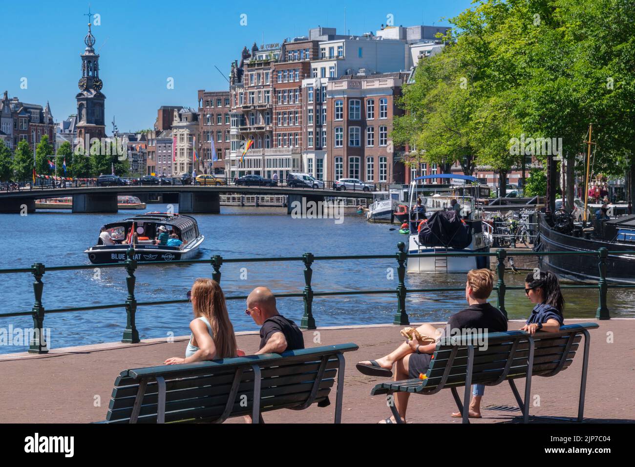 Amsterdam, Paesi Bassi - 22 giugno 2022: Persone sedute su panchine sul lungomare del fiume Amstel Foto Stock