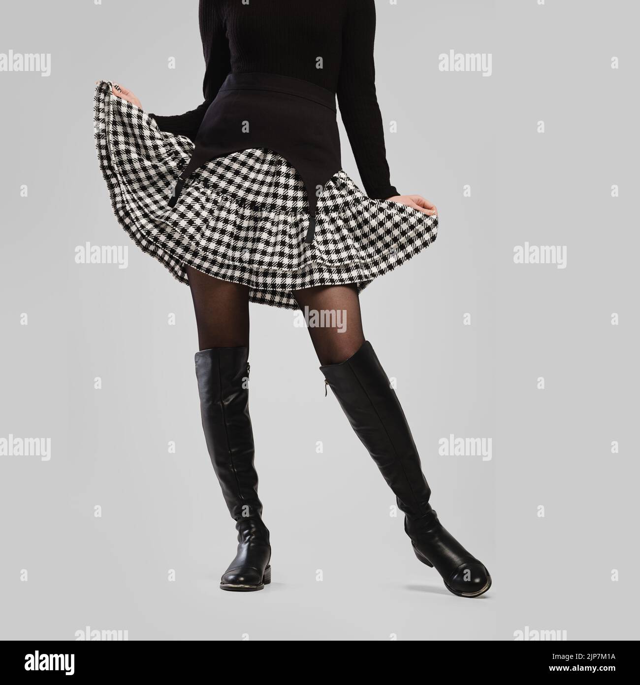 Gambe femminili sottili in stivali alti e gonna piccola su sfondo grigio Foto Stock