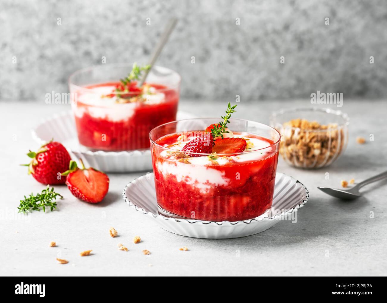 Due bicchieri con dessert estivo freddo. Salsa di fragole e crema di yogurt decorata con frutti di bosco freschi, muesli e foglie di timo al limone. Homemad Foto Stock