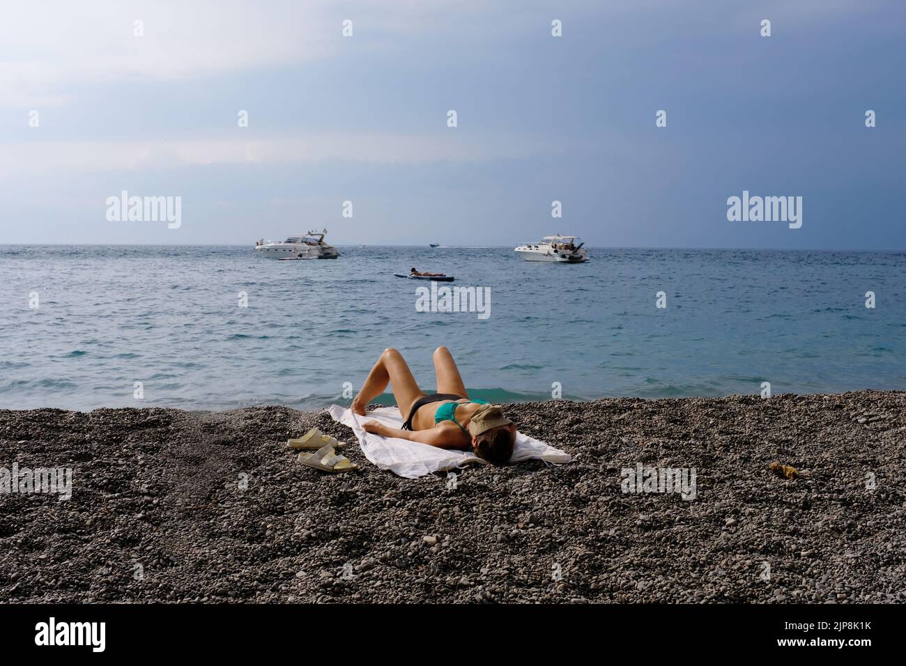 Una donna che prende il sole su una spiaggia pubblica a vico equense italia con le barche sullo sfondo. Foto Stock