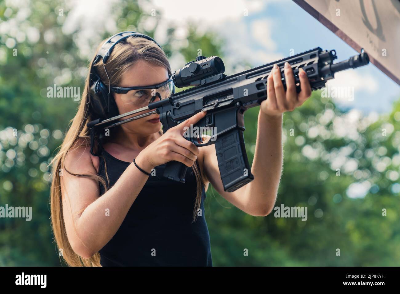 Giovane donna caucasica che indossa occhiali protettivi e cuffie che pratica con una pistola sottomaratrice sul campo di tiro all'aperto. Scatto orizzontale. Foto di alta qualità Foto Stock