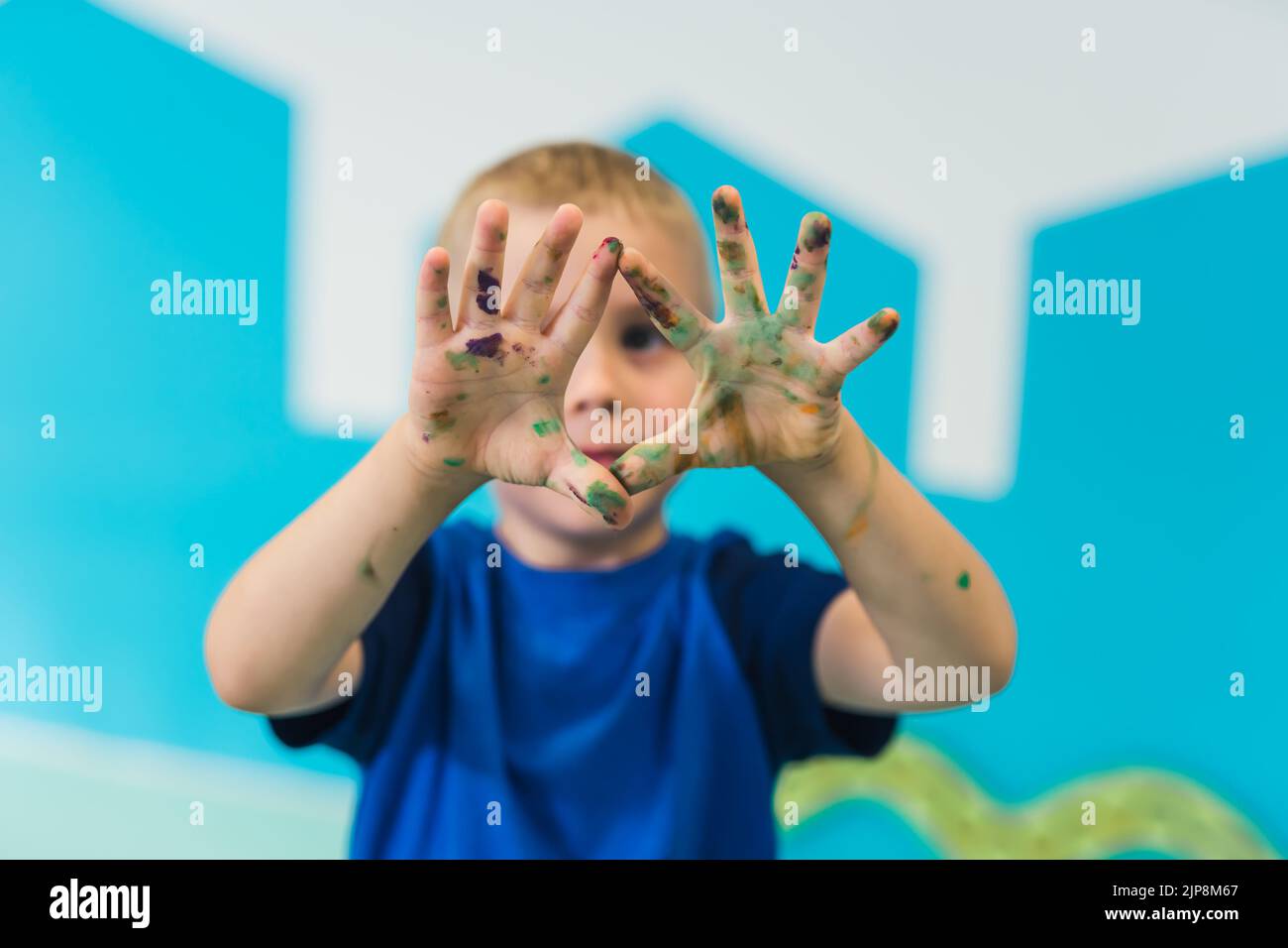 Scuola materna. Ragazzo biondo carino che mostra le sue palme colorate dipinte. Classe d'arte con pittura a dita per bambini abilità sensoriali, creatività e sviluppo di immaginazione Foto Stock