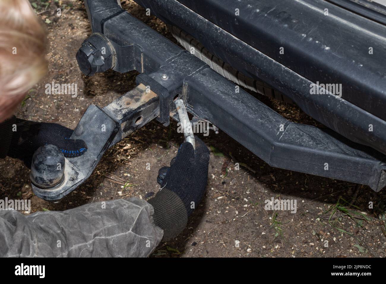 Un uomo monta una barra di traino in ferro su un'auto per trainare un rimorchio. Dispositivo per il trasporto. Foto Stock