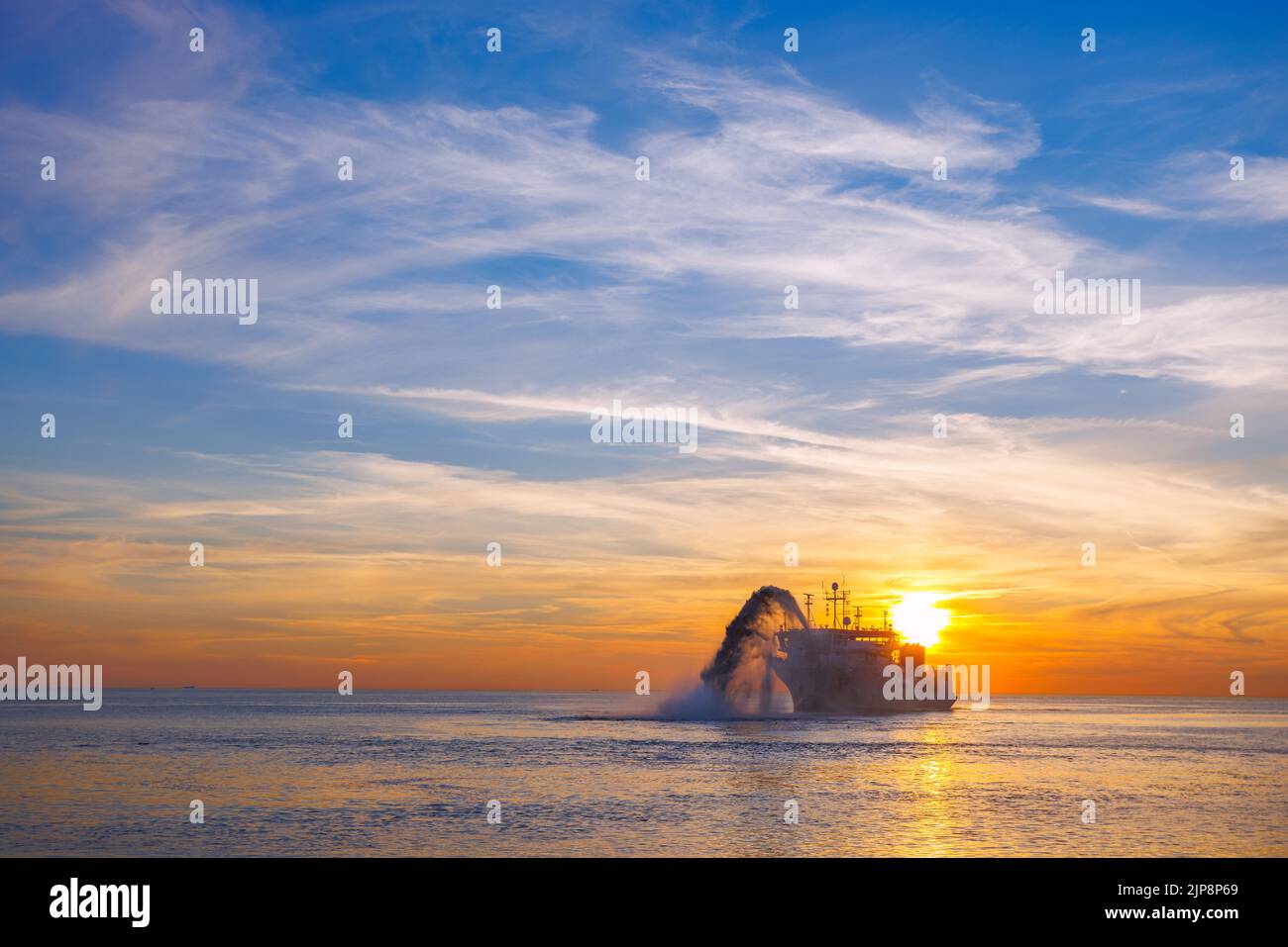 Nave impegnata in dragaggio al tramonto. Draga tramoggia funzionante in mare. Spedire il materiale di scavo da un ambiente idrico. Bellissimo tramonto, Baltico Foto Stock