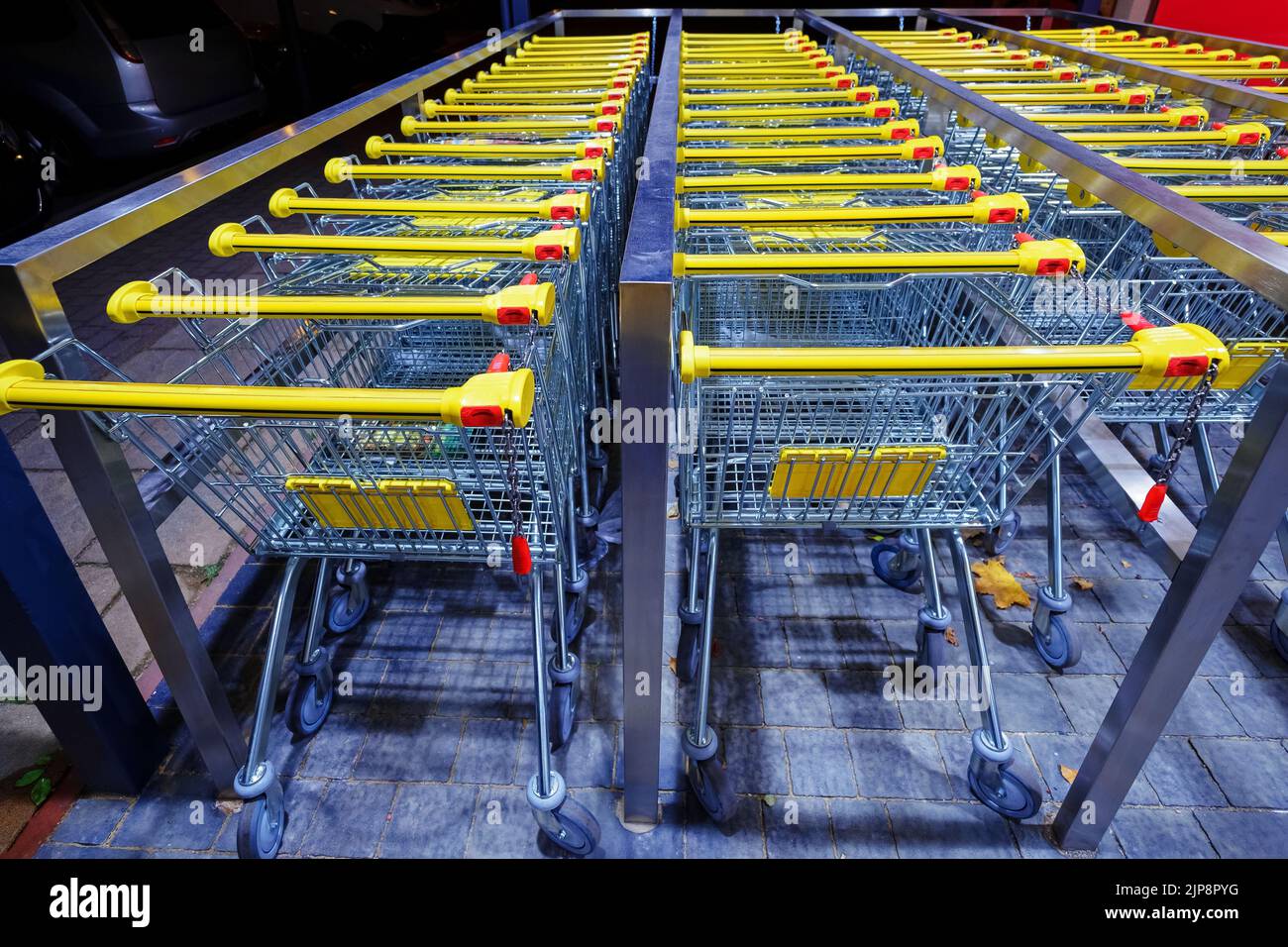 Fila di carrelli in metallo impilati con maniglie gialle vicino al supermercato Foto Stock