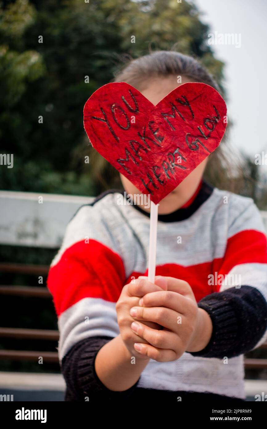 Febbraio 14th 2021. Dehradun India. Buon San Valentino. Un capretto indiano carino che tiene la scheda rossa a forma di cuore con una citazione d'amore 'il vostro Make My Heart Foto Stock