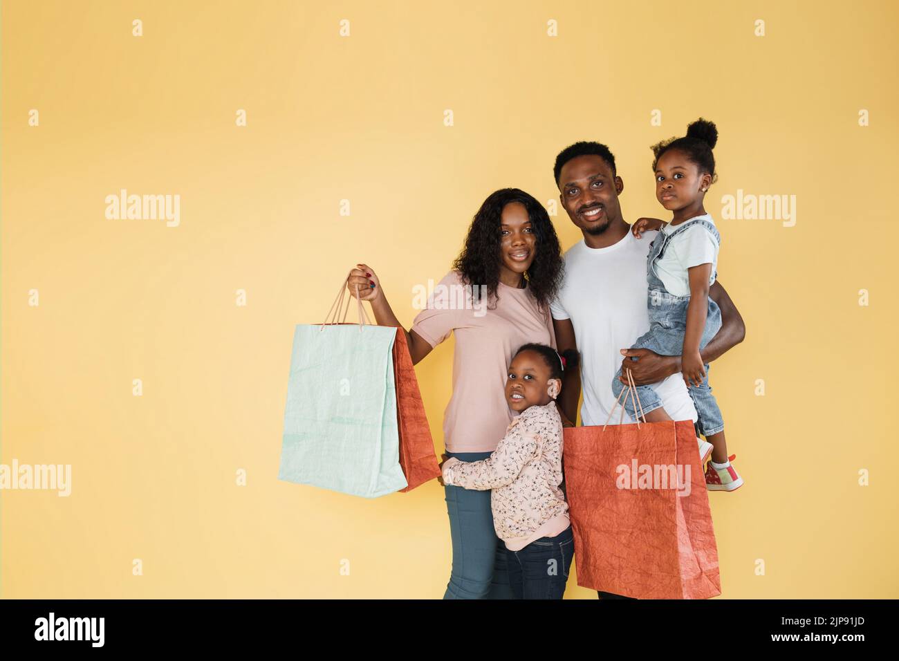 Giovane felice divertimento genitori mamma papà con due bambini figlie ragazze in abiti casual in possesso di borse pacchetto acquisti dopo lo shopping isolato su sfondo giallo. Foto Stock