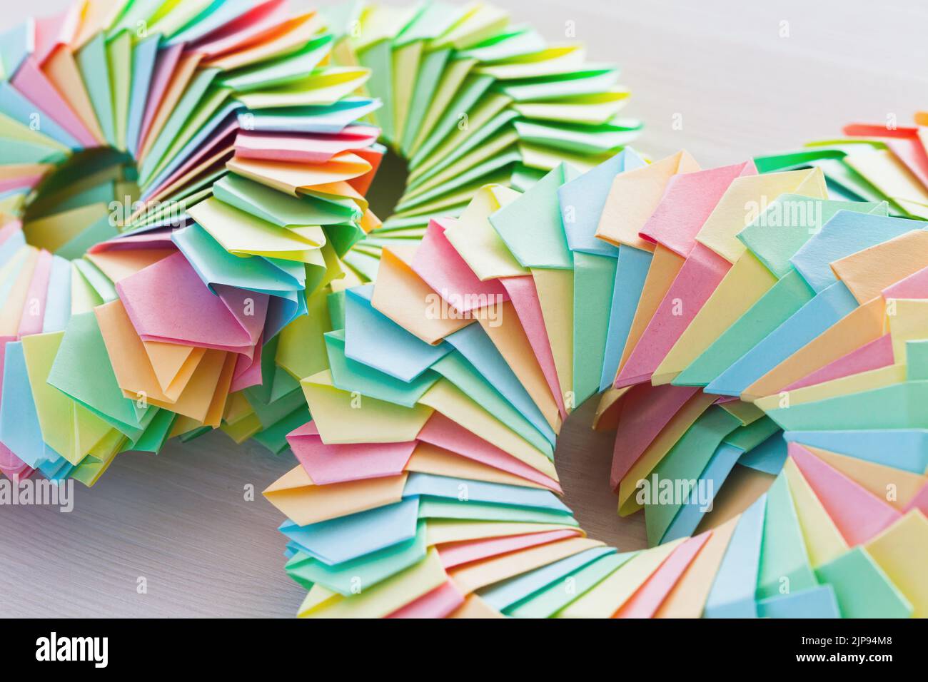 Gli anelli Origami in fogli di carta colorati collegati giacciono su un tavolo di legno bianco, foto ravvicinata con messa a fuoco morbida selettiva Foto Stock