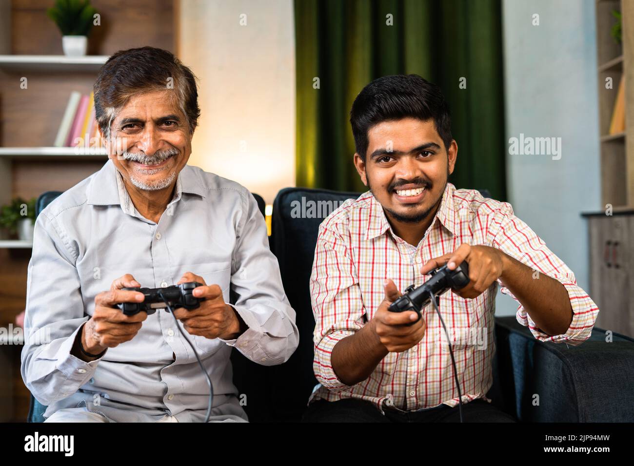 Buon nonno sorridente e nipote che gioca a un videogioco usando il game pad guardando la fotocamera a casa - concetto di intrattenimento, legame familiare e. Foto Stock