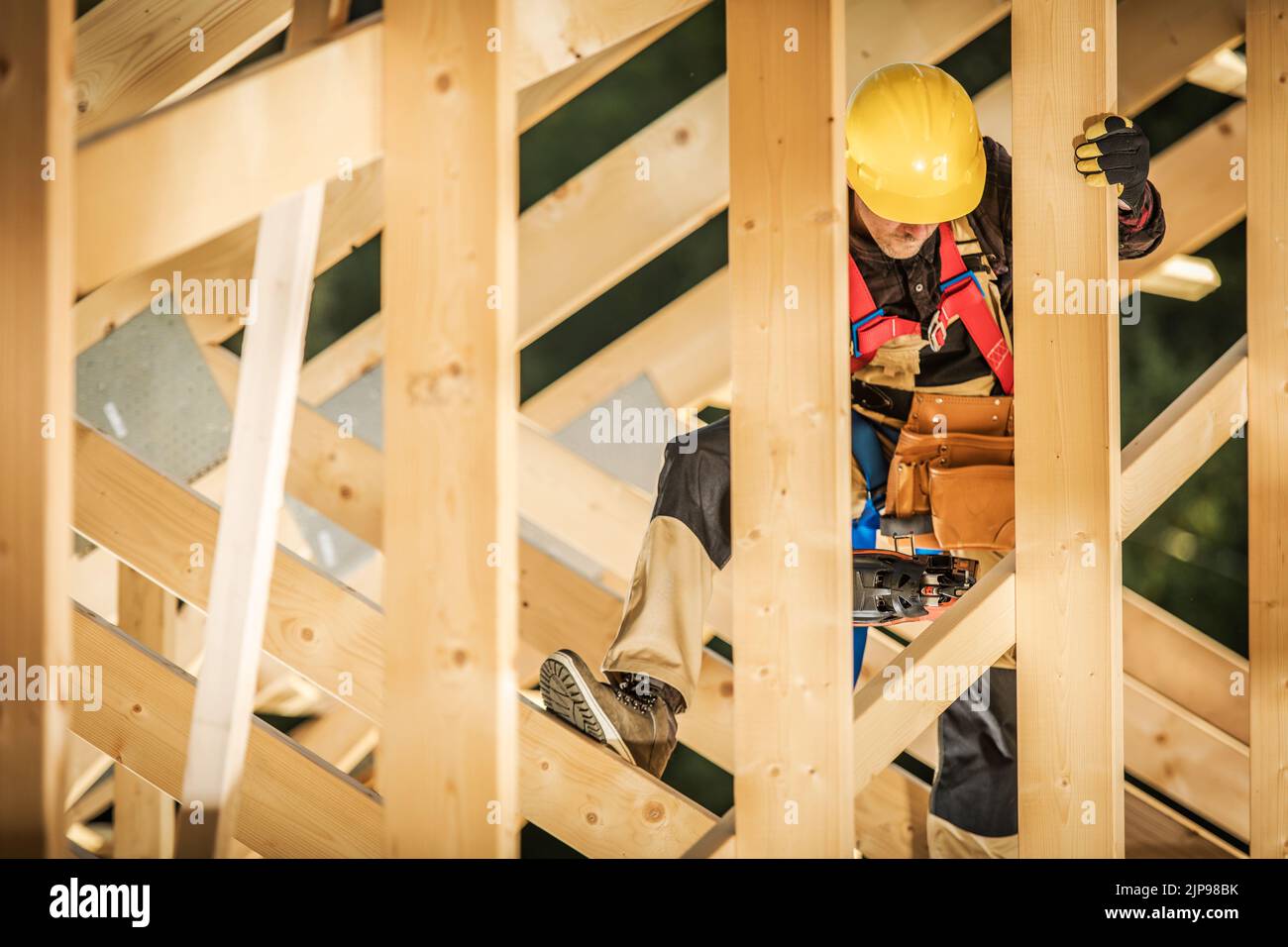 Costruttore completamente attrezzato che lavora con assi in legno nella sezione del tetto di stile canadese edificio residenziale in costruzione. Tema industriale. Foto Stock