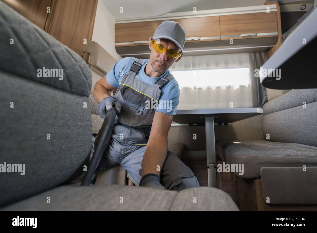 Lavoratore caucasico maschio prendersi cura di Camper Van interni pulendo il mobili con aspirapolvere. Preparativi per la stagione in campeggio. Veicoli ricreativi Foto Stock
