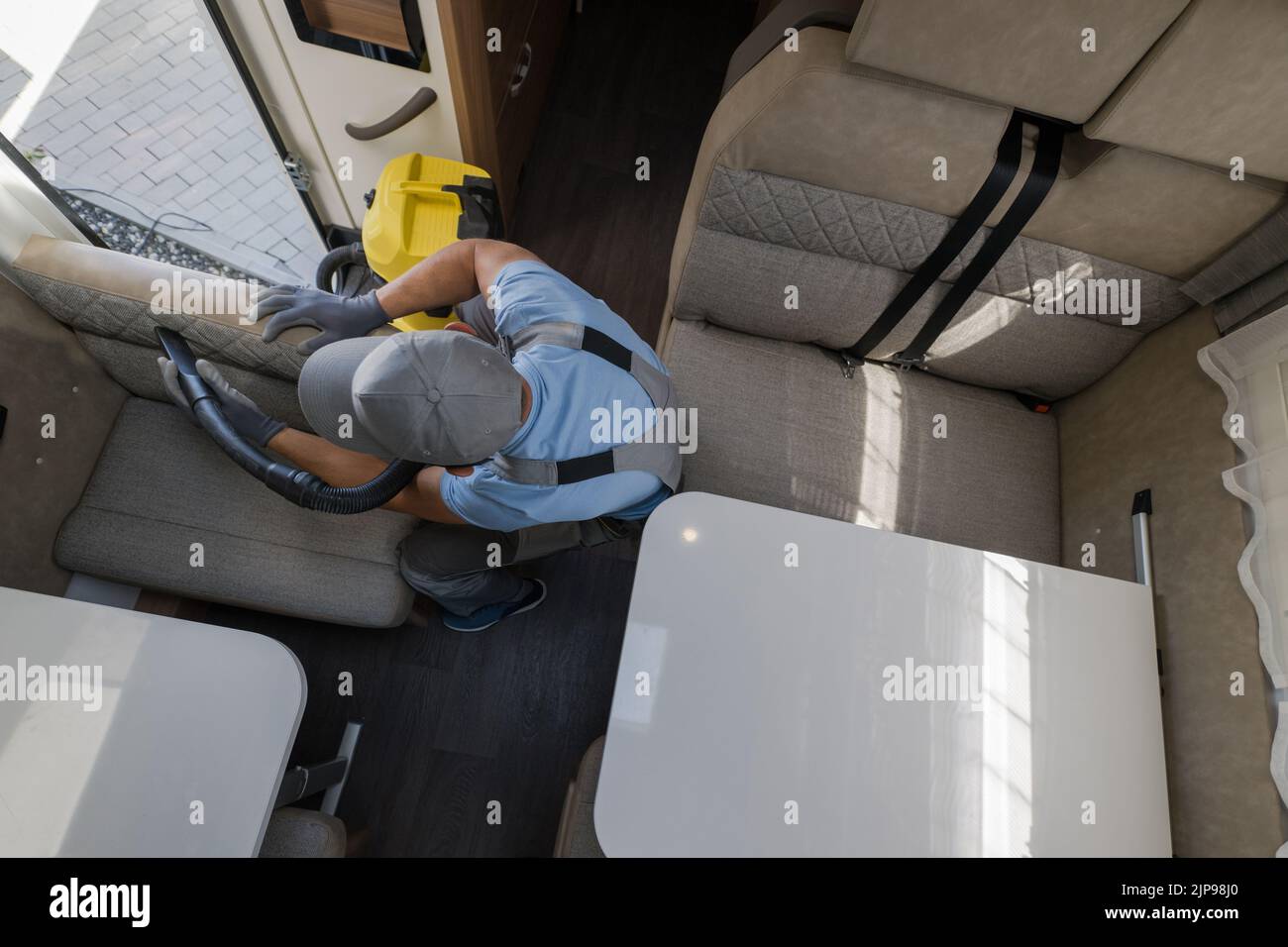Vista aerea di Caucasian pulizia servizi lavoratore con cura Vacuuming il tessuto finitura della zona soggiorno nel moderno veicolo ricreativo. Auto RV Foto Stock