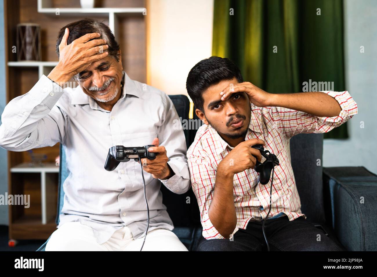 Padre e figlio entusiasti si sono tristi durante il gioco video utilizzando gamepad a causa di perdita - concetto di intrattenimento, vacanze fine settimana e tempo per la famiglia. Foto Stock