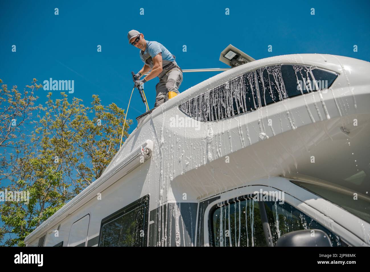 Uomo caucasico lavare il suo Motorhome bianco mentre in piedi sulla cima del suo tetto. Proprietario di un camper che si prende cura del suo veicolo dopo un lungo viaggio. Foto Stock