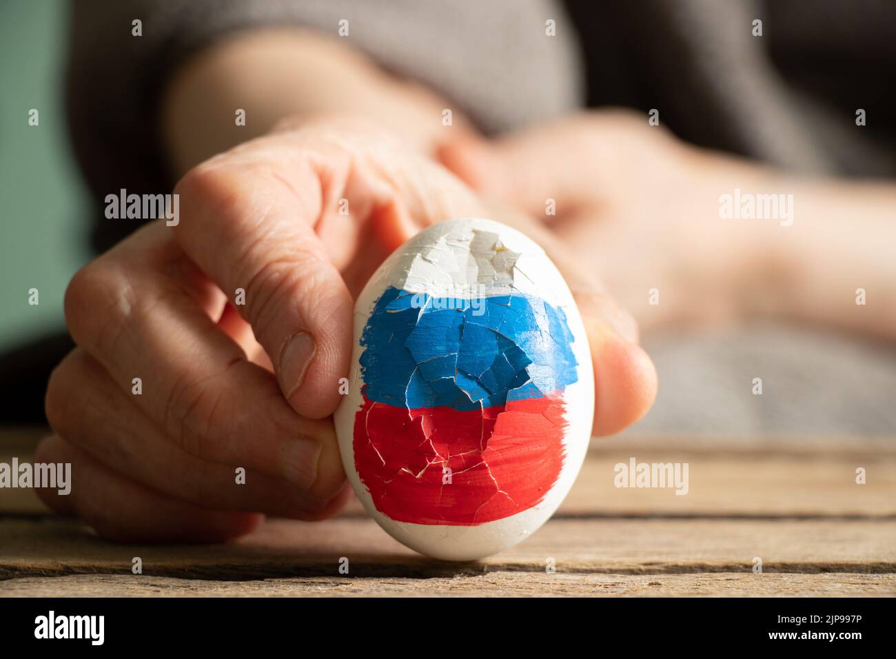 Un uovo bianco con una bandiera dipinta della Russia è rotto nelle mani di una donna, vacanza di Pasqua, la Russia è rotto e perso la guerra 2022 Foto Stock