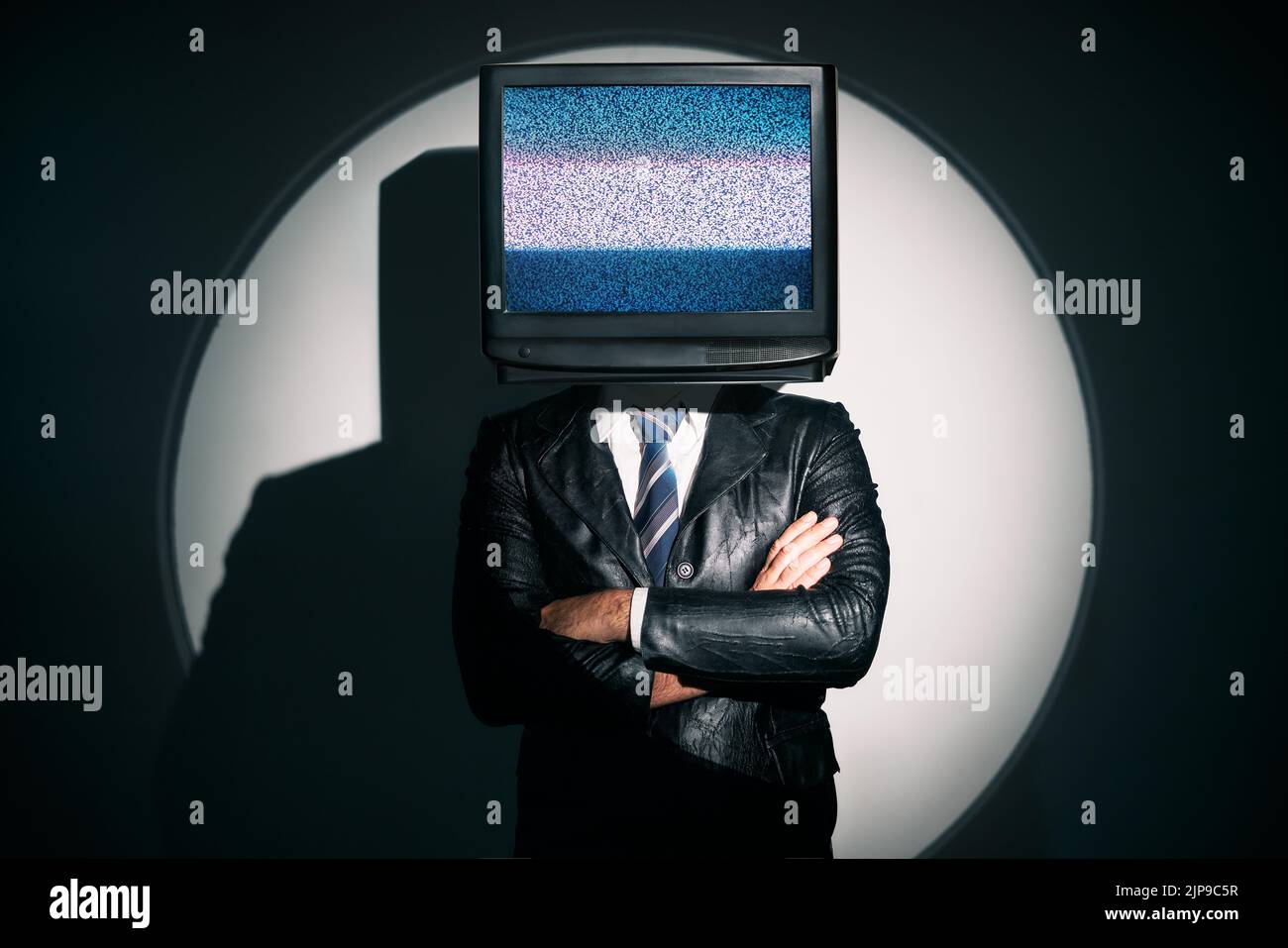 Uomo con la TV invece della testa. Media zombie concetto con televisione addicted maschio in nero cappotto con braccia incrociate in posa in studio sotto i riflettori. Con Foto Stock