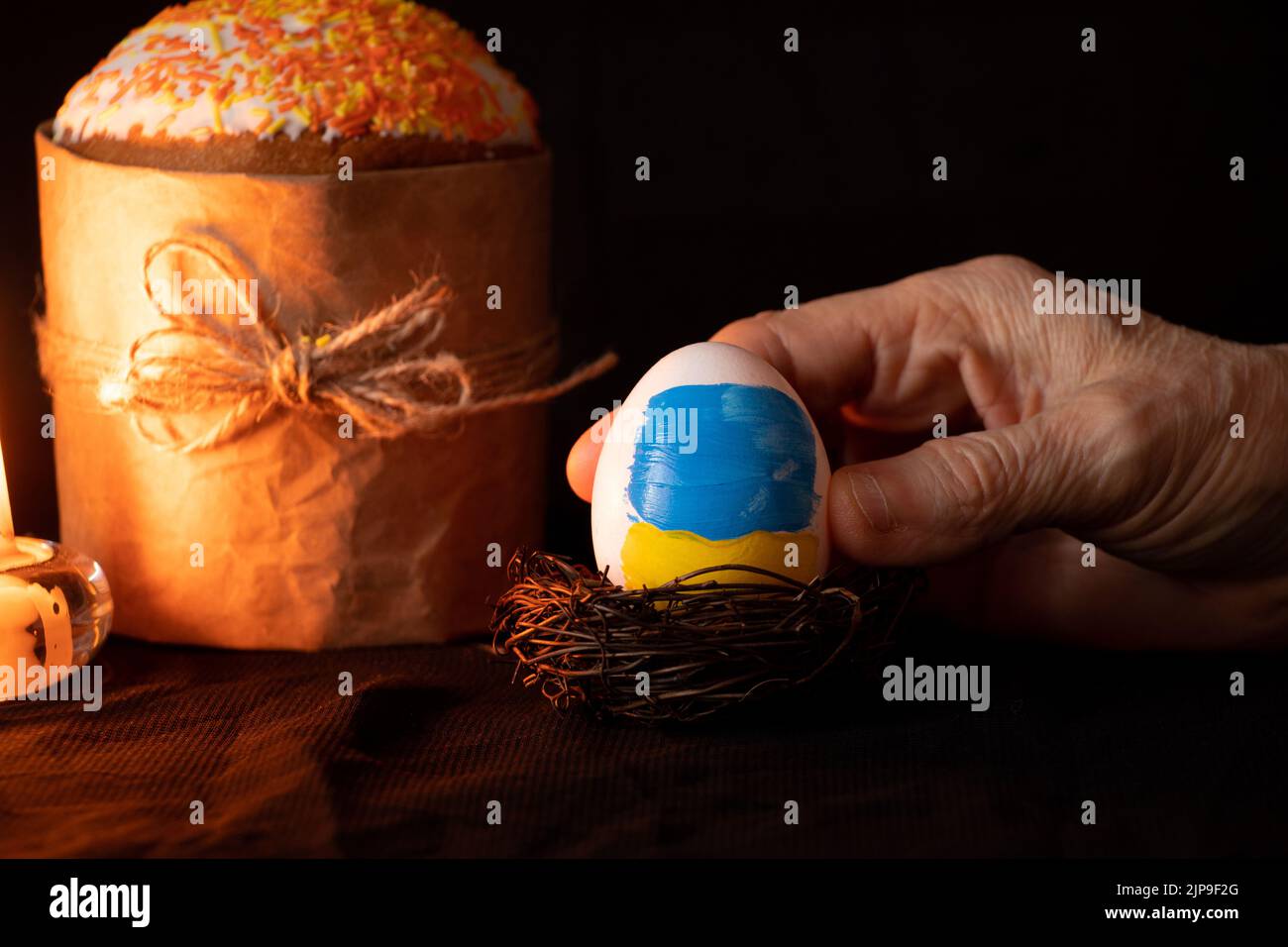 Torta di Pasqua e accanto a un uovo con una bandiera dipinta di Ucraina nelle mani di una donna su uno sfondo nero, candele, vacanze di Pasqua in Ucraina durante Foto Stock
