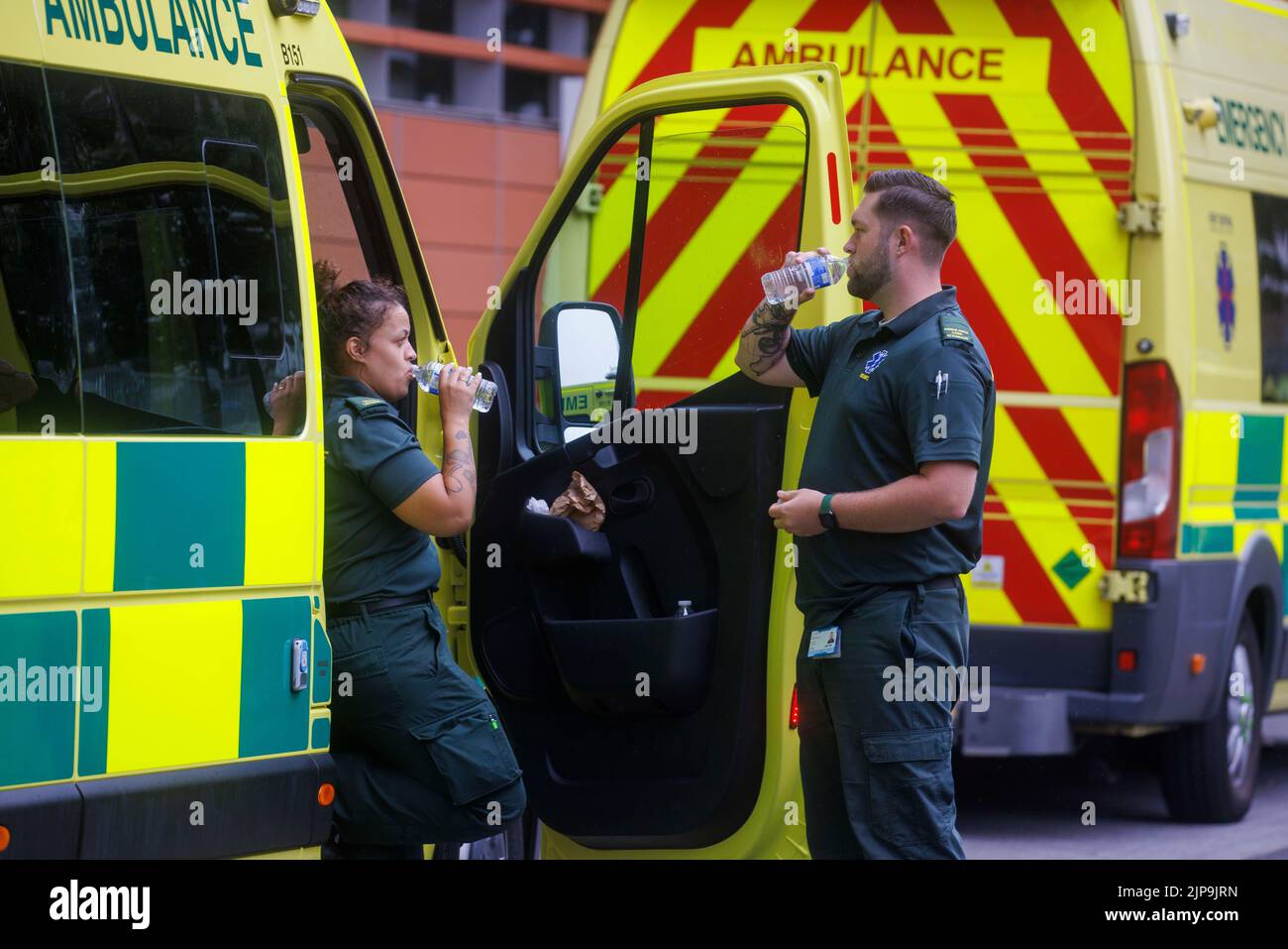 Due operatori dell'ambulanza prendono una pausa durante un turno durante il tempo caldo di estate. Il servizio di ambulanza è sotto pressione con un carico di lavoro aumentato. Foto Stock