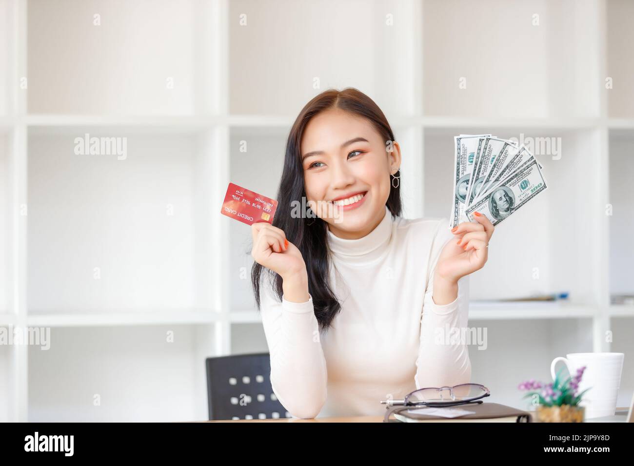 Donna asiatica in possesso di carte di credito e dollari sensazione felice con lo shopping online. Foto Stock