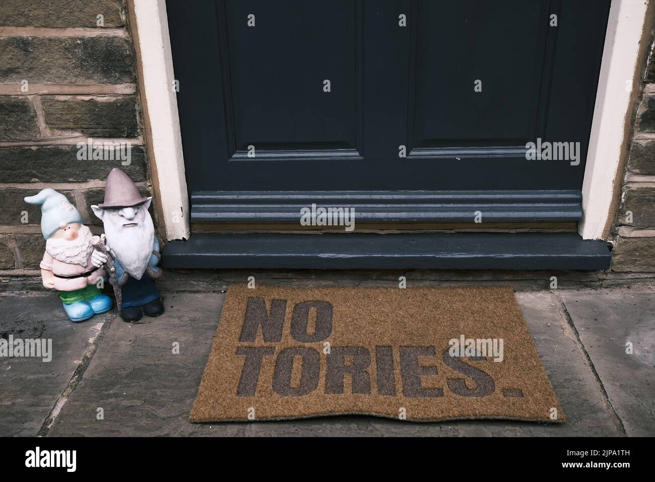 Tappeto politico porta con 'No Tories' stampato all'esterno di una casa con due gnomi nelle vicinanze. Foto Stock