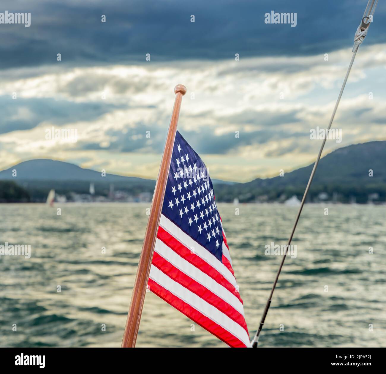 Una bandiera americana a poppa di una barca a vela con un lontano Camden Maine sullo sfondo Foto Stock