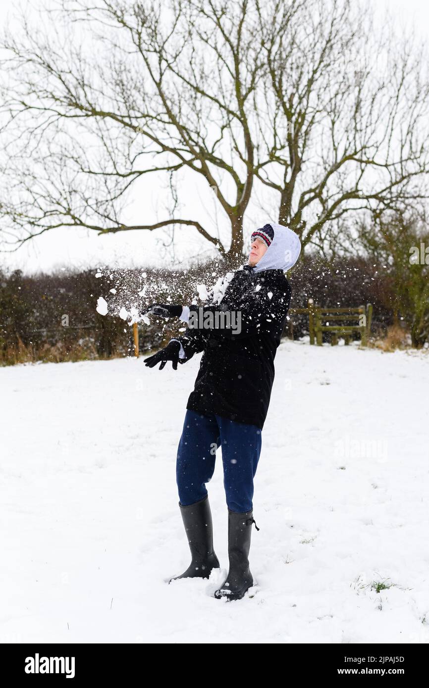 Un uomo caucasico che gioca a combattimenti sulla neve nel cortile posteriore durante una giornata invernale innevata Foto Stock