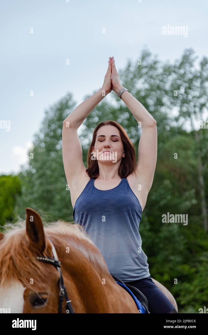 giovane donna che fa yoga su un cavallo sullo sfondo di alberi Foto Stock