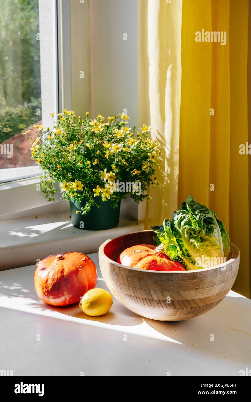 Verdure - Punpkin, insalata verde - in una ciotola di bambù su un tavolo bianco di fronte alla finestra con luce naturale. Luce solare. Concetto di zero sprechi. Acquista cibo biologico locale Foto Stock