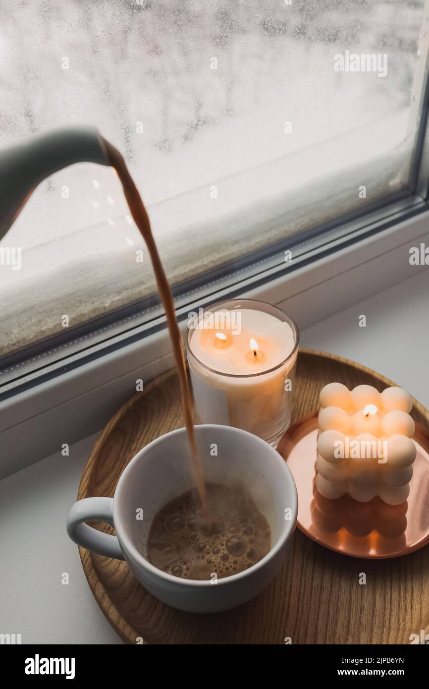 Inverno ancora vita con bevande calde e candele. Versare cacao caldo o caffè con latte in una tazza Foto Stock
