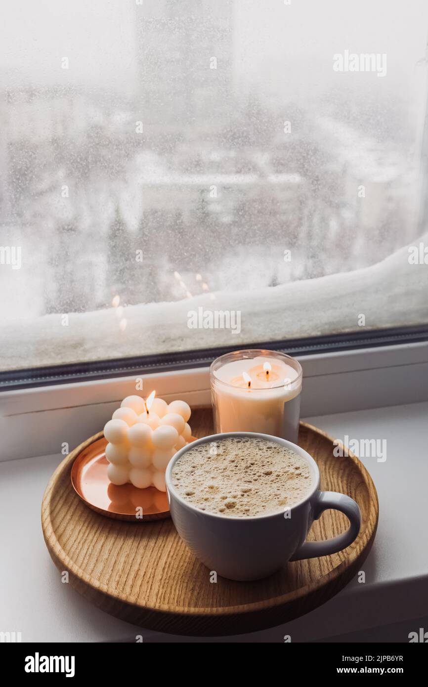 Atmosfera accogliente inverno ancora vita con bevande calde e candele sul davanzale, con neve sullo sfondo. Foto Stock