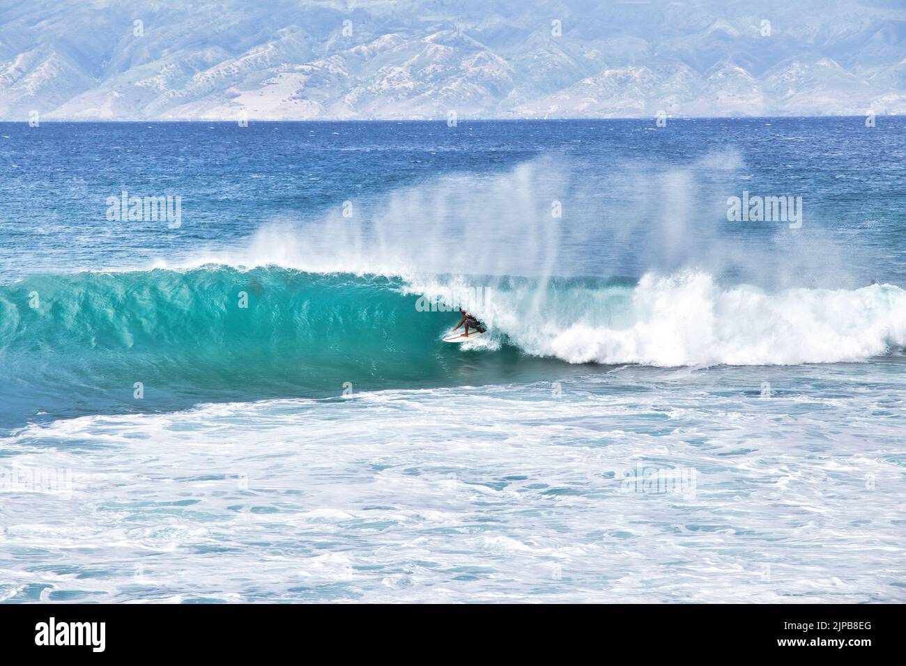 Distanrt scatto di un surfer non identificabile nascosto nel tubo di un'onda di rottura. Foto Stock