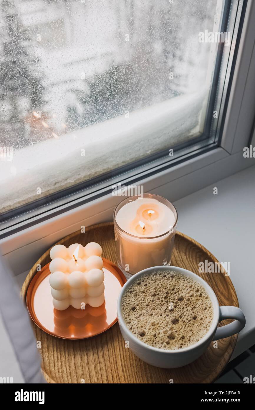 Atmosfera accogliente inverno ancora vita con bevande calde e candele sul davanzale, con neve sullo sfondo. Foto Stock