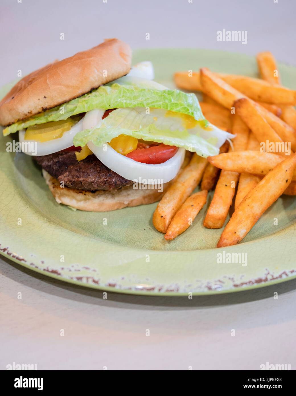 Un hamburger cotto su un panino con senape, cipolla, pomodoro, sottaceti e lattuga, con patatine fritte o patatine fritte. STATI UNITI. Foto Stock