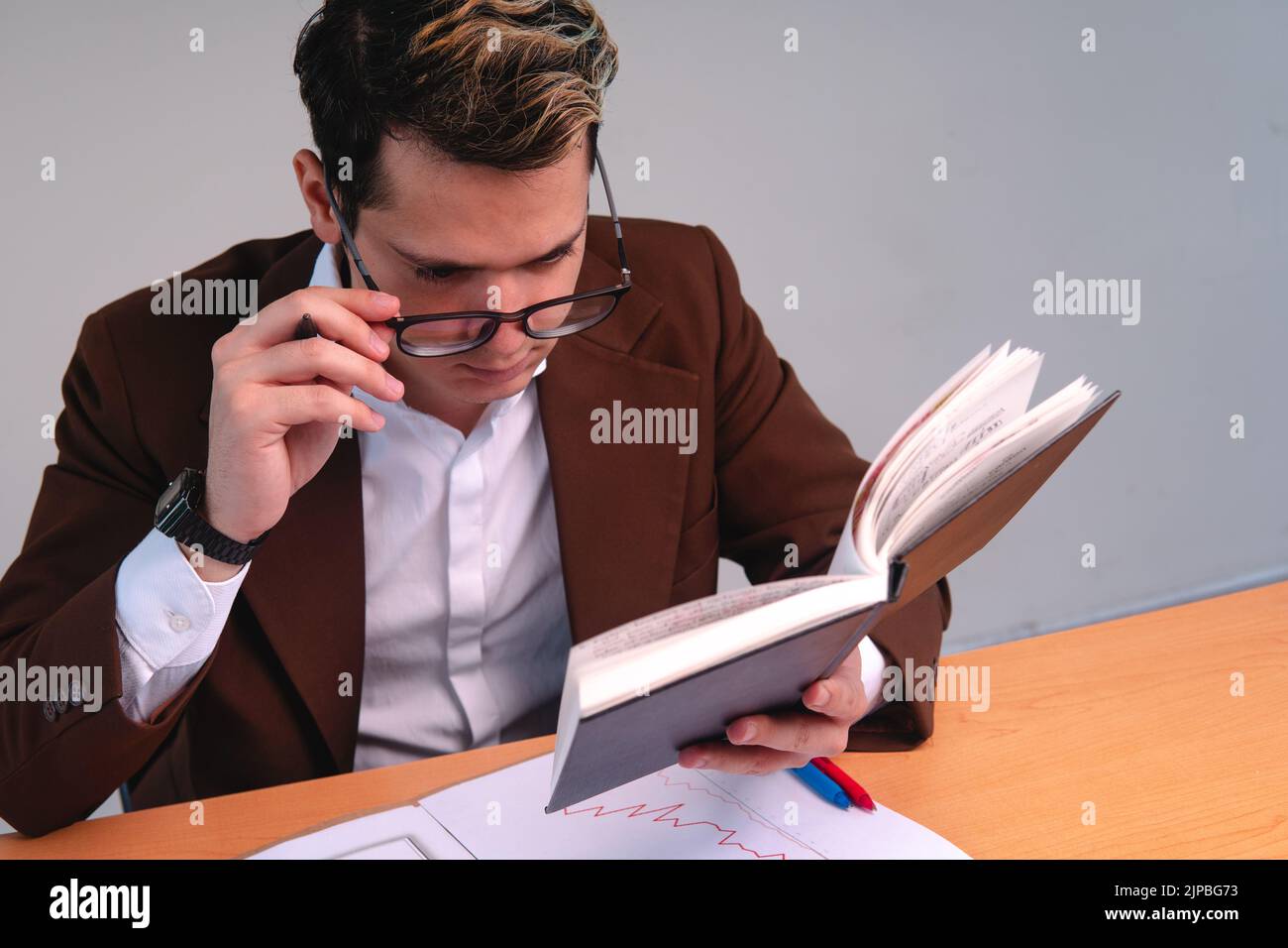 Uomo elegante concentrato che legge alla sua scrivania su uno sfondo bianco. Uomo biondo caucasico che legge nel suo ufficio. Uomo d'affari che lavora nel suo ufficio. Foto di alta qualità Foto Stock