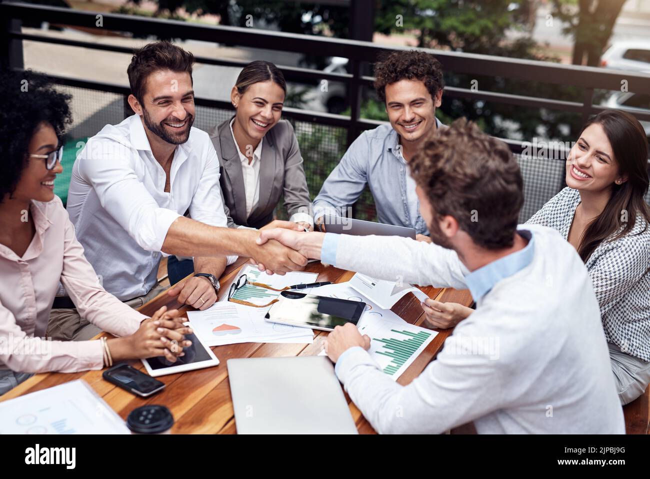 Benvenuti nel team. Due bei giovani uomini d'affari scuotono le mani mentre si siedono con i colleghi all'aperto. Foto Stock