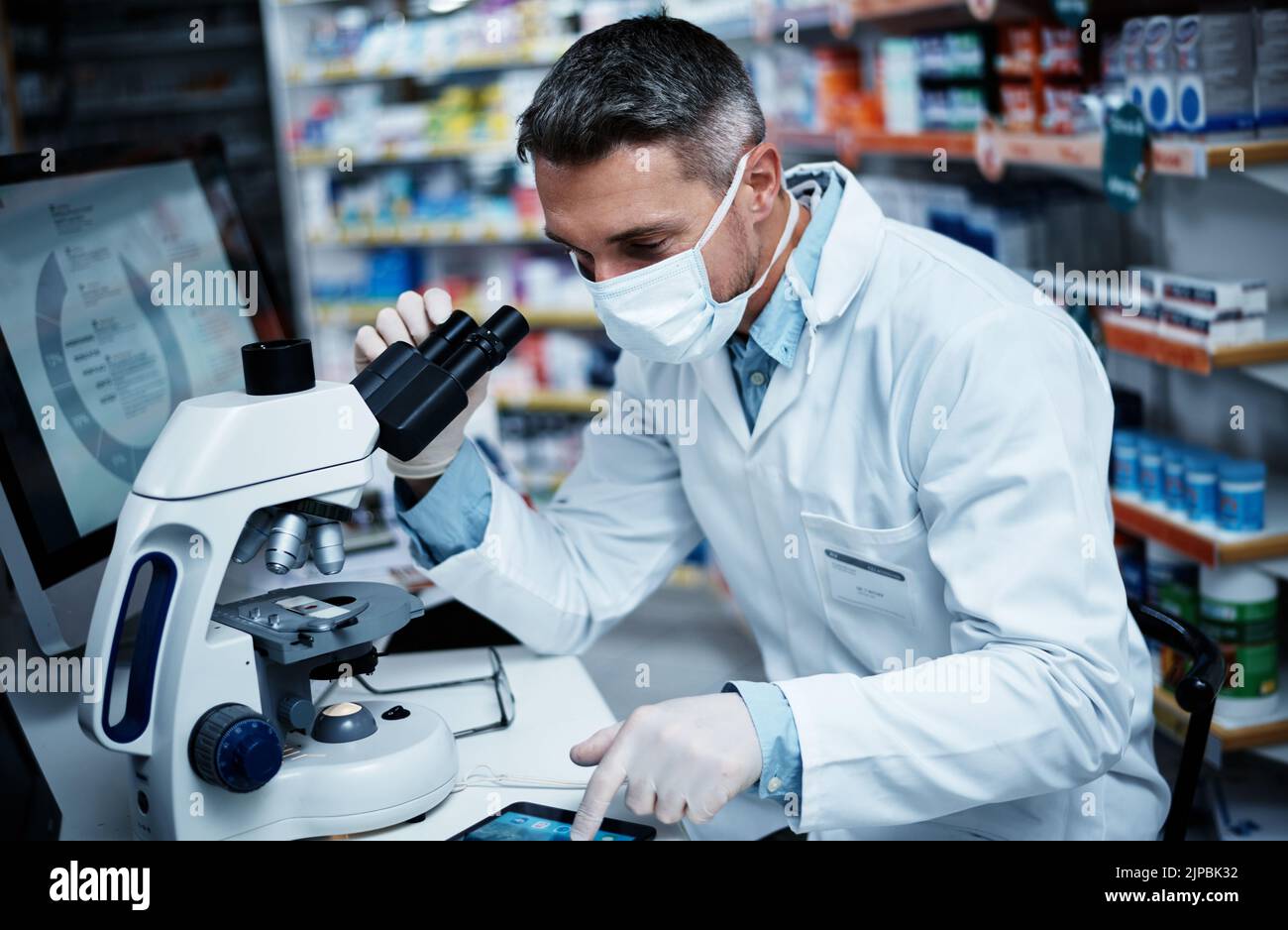 Il microscopio rivela tutto. Un uomo maturo che usa un microscopio e una compressa digitale mentre conduce la ricerca farmaceutica. Foto Stock