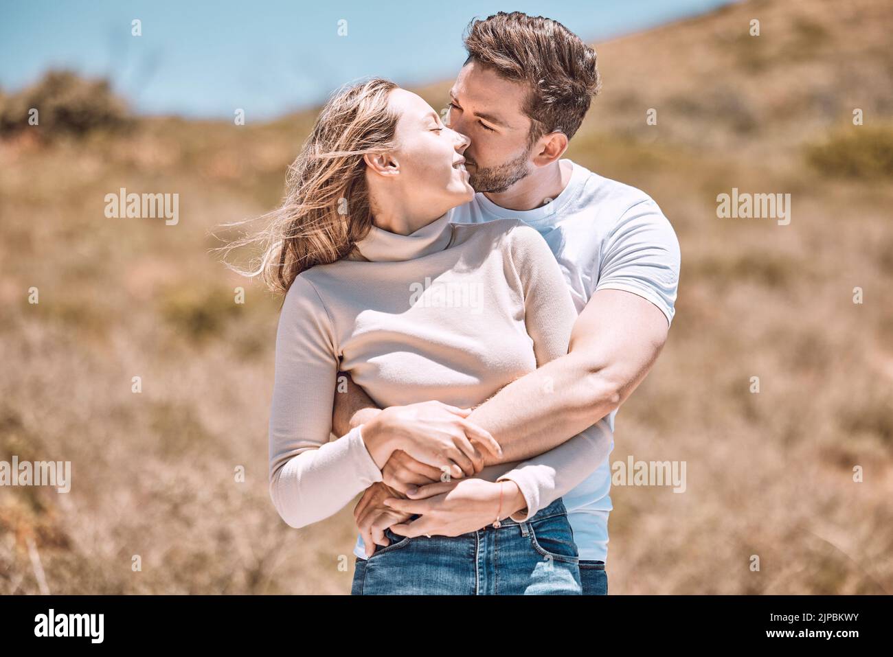 Abbracciando, abbracciando e innamorando giovani coppie che trascorrono insieme una romantica giornata estiva nella natura. Partner felici in una fuga baciando, sorridendo e. Foto Stock