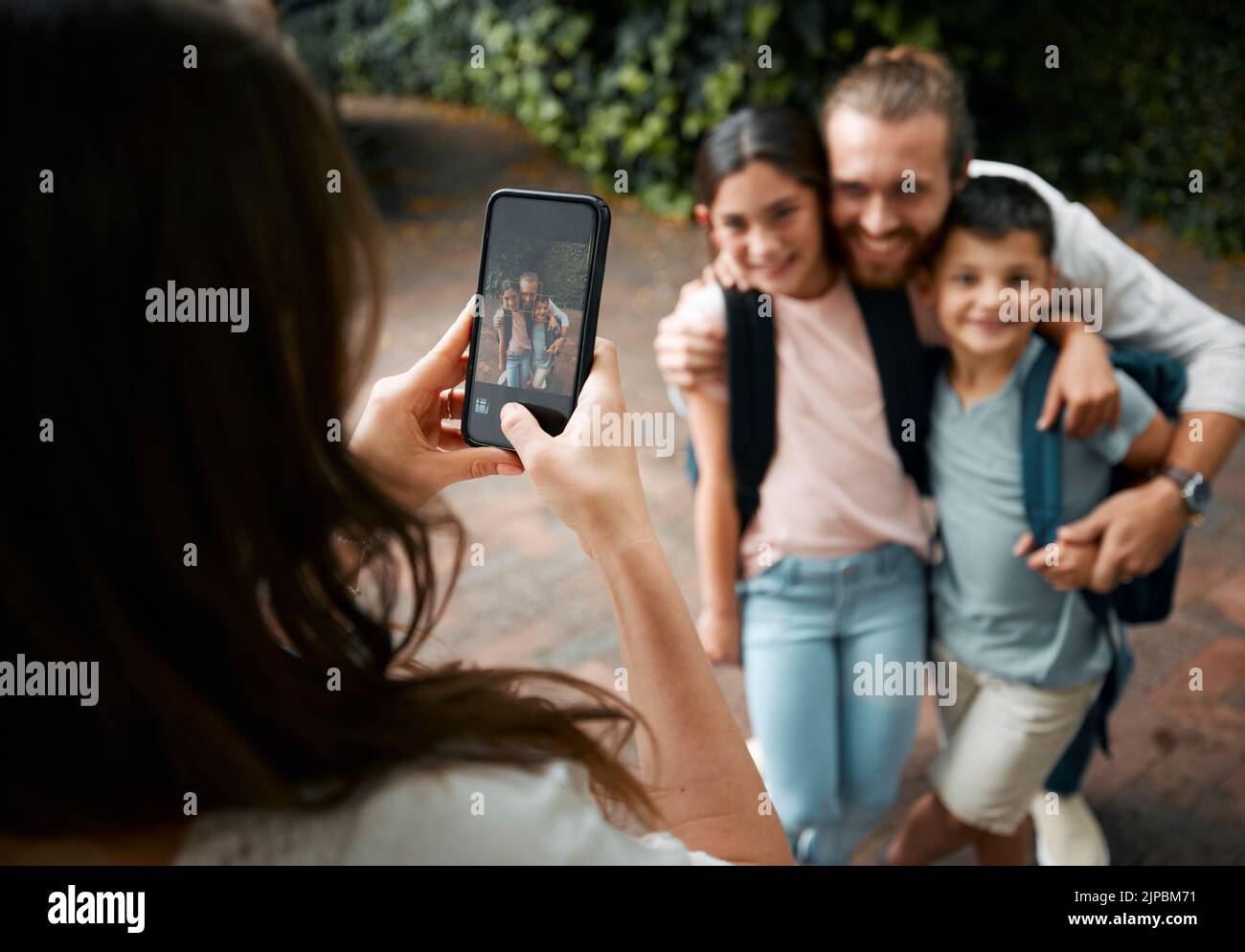 Madre che scatta una foto di famiglia sul suo telefono dei suoi bambini felici e del loro padre che sorride prima della scuola. Ragazzo e ragazza fratelli con il loro papà Foto Stock