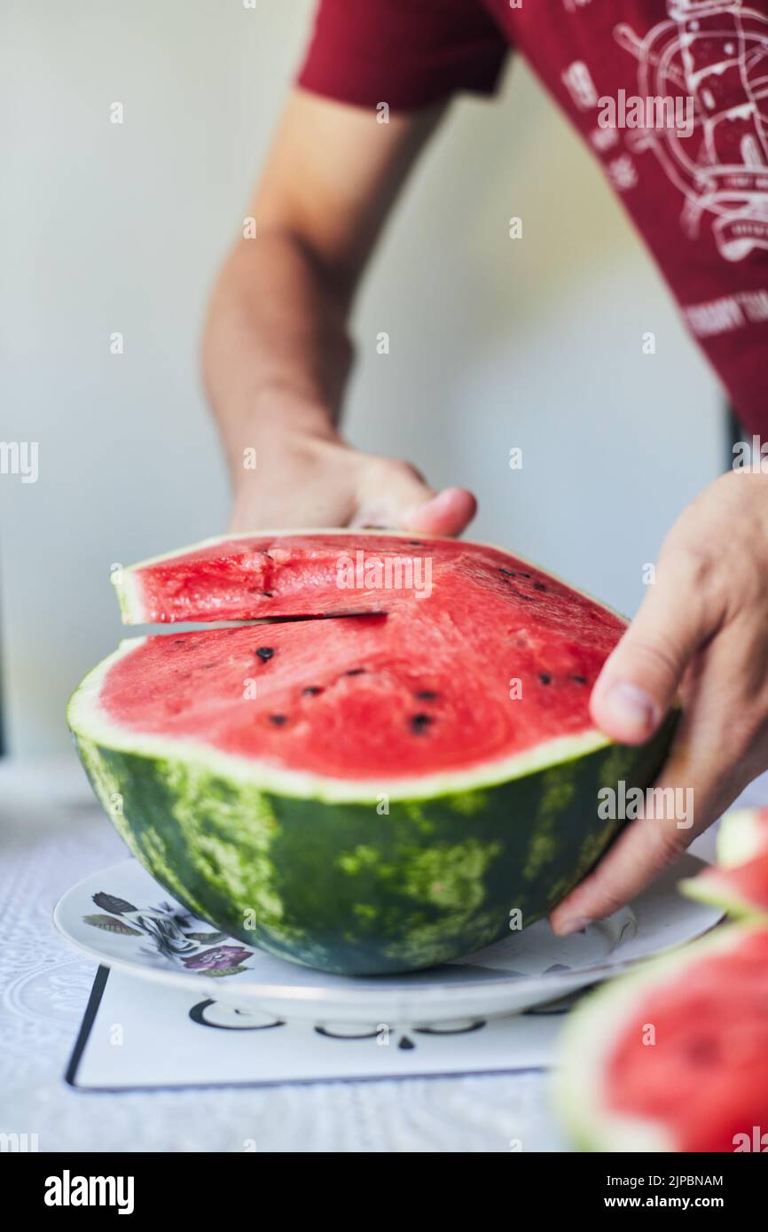 Il cocomero rosso succoso viene tagliato con un coltello. Il concetto di estate e verdure deliziose. Foto verticale. Foto Stock